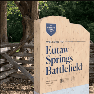 Eutaw Springs Battlefield sign with trees and wooden fence in background.