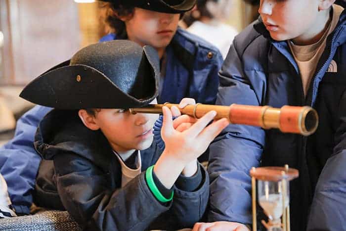A child in a tricorn hat looks through a replica historical telescope.