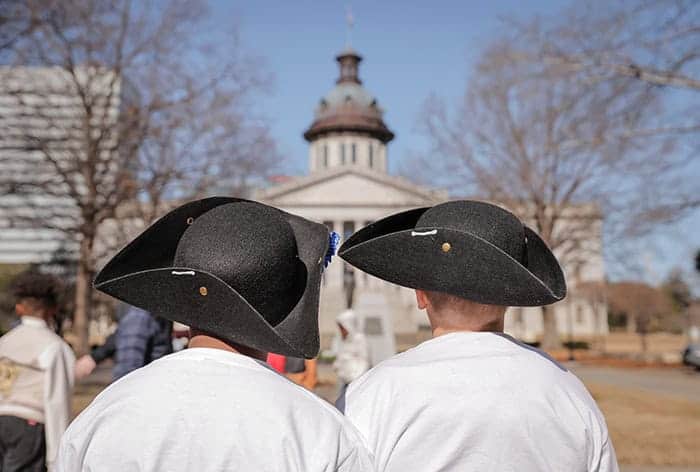 Two visitors in colonial-style tricorn hats face the South Carolina State House.